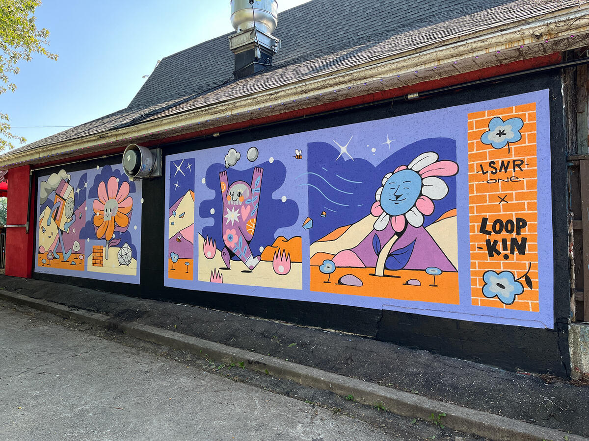 Murale par les artistes Lucas Saenger et Loopkin sur le mur du restaurant Patate Rouge. On y voit des personnages joyeux et colorés en forme de fleurs et de maisons.