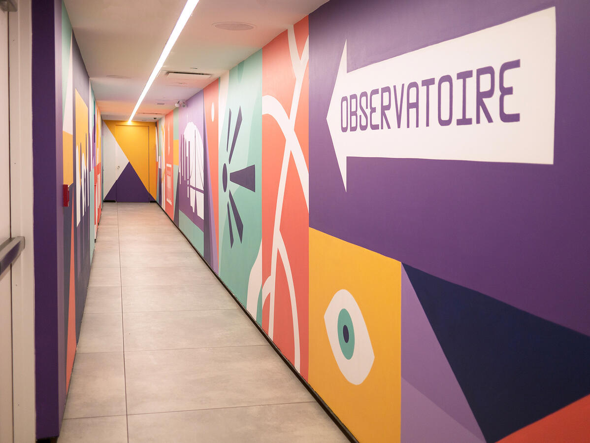Une murale peinte dans le couloirs vers l'observatoire de la place Ville-Marie par Lucas Saenger. Une composition en blocs de couleurs représentant des éléments de la ville et des symboles.