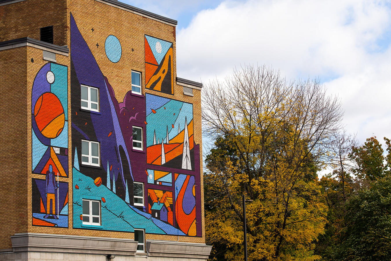 Murale peinte par Lucas Saenger au centre-ville de Trois-Rivières. Une composition colorée représentant un marcheur en montagne qui contemple la vue.